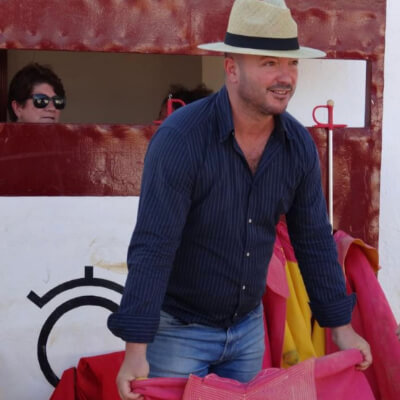 A man in a blue shirt, white hat, and jeans holding pink clothing material